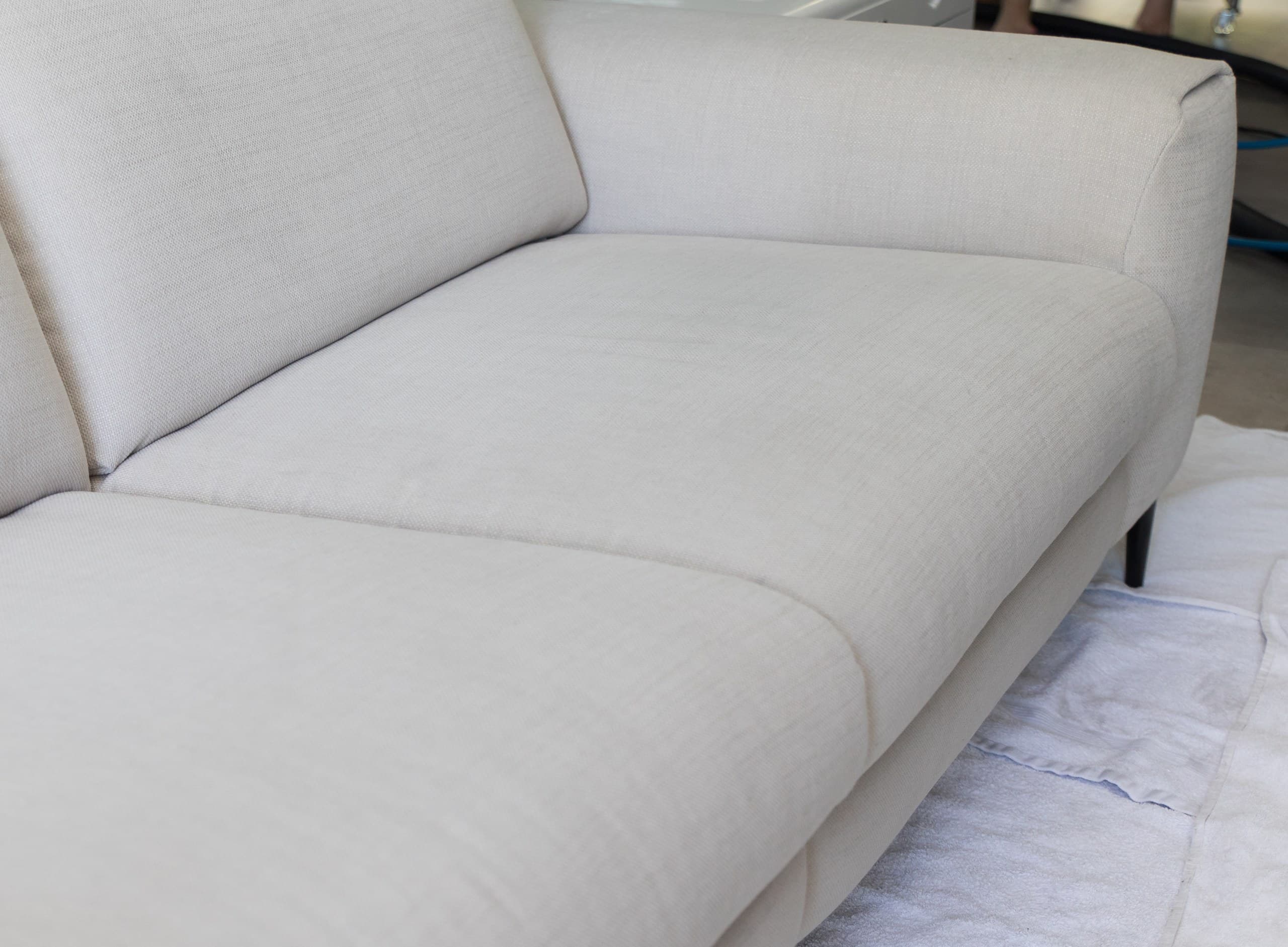 Beige stoffen bank met schoon zitkussen tijdens meubelreiniging op beschermdoek